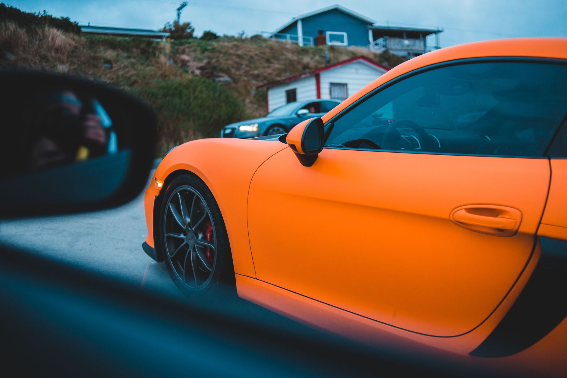 Contemporary luxury orange automobile with tinted glass near hillside with cottages in countryside