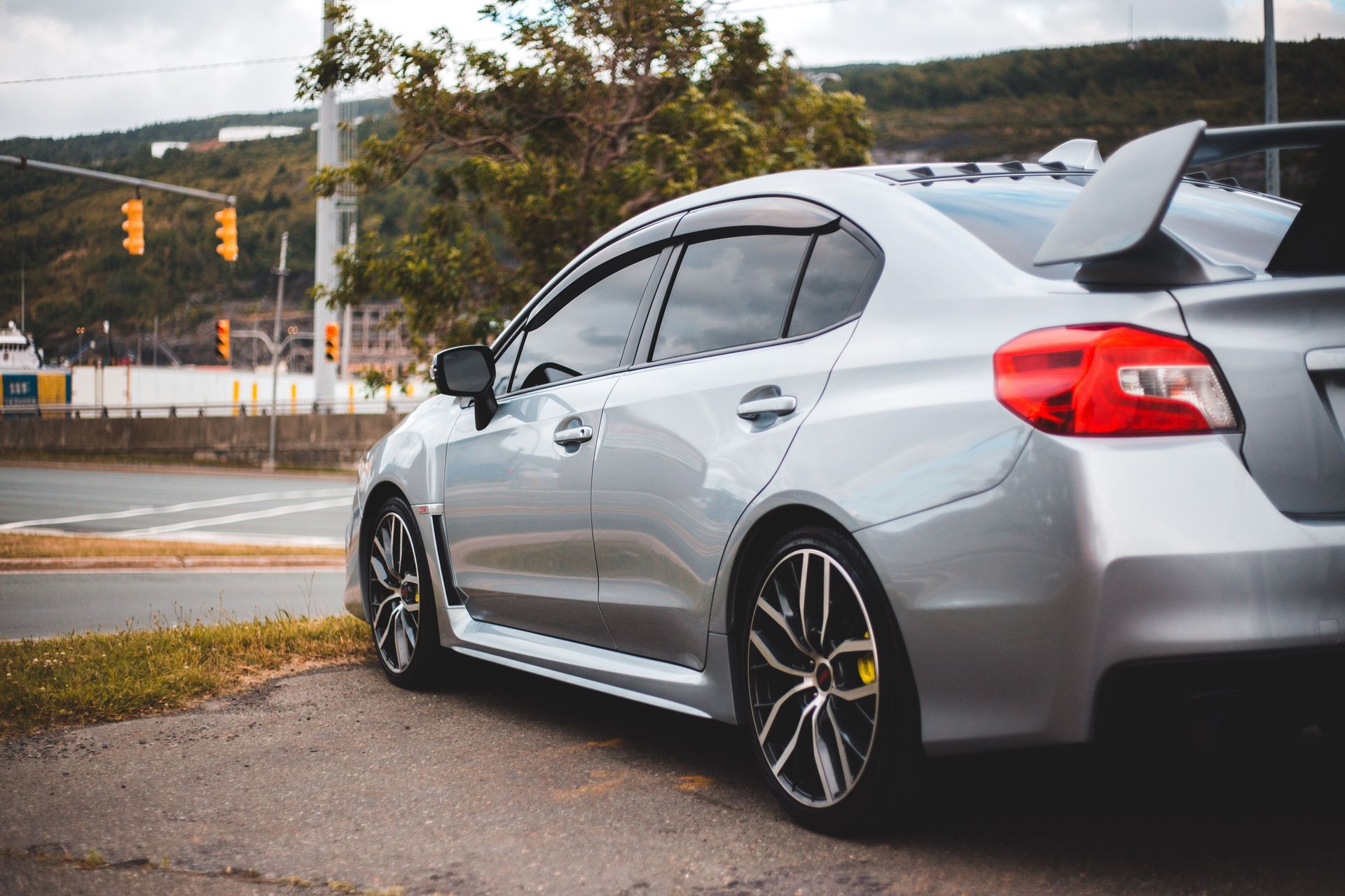 Silver sporty car with spoiler parked on an urban street, showcasing sleek design and modern automotive features.